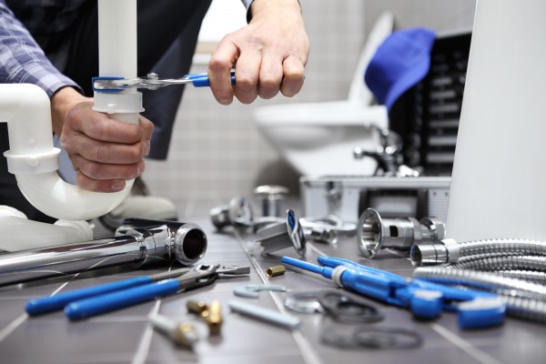 A plumber is surrounded by parts and tools as he repairs a sink pipe