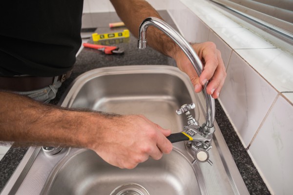 Plumber replacing the sink faucet with wrench
