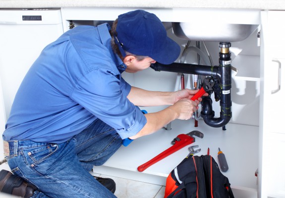 Plumber in a blue shirt fixes a sink pipe